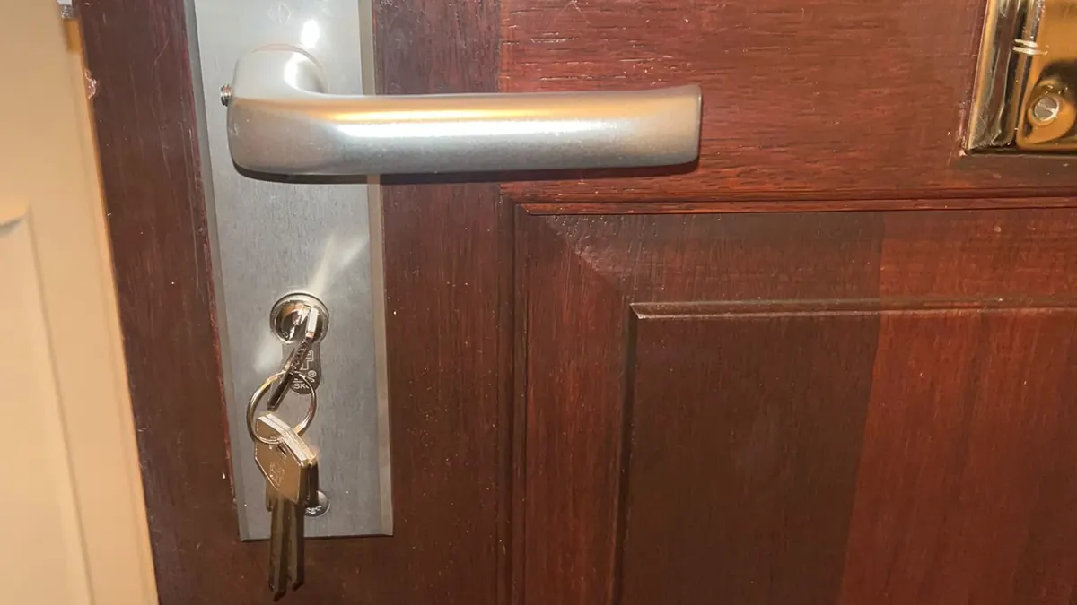 Sleutelbos in de cilinder aan de binnenkant van een houten voordeur, onder een aluminium deurkruk