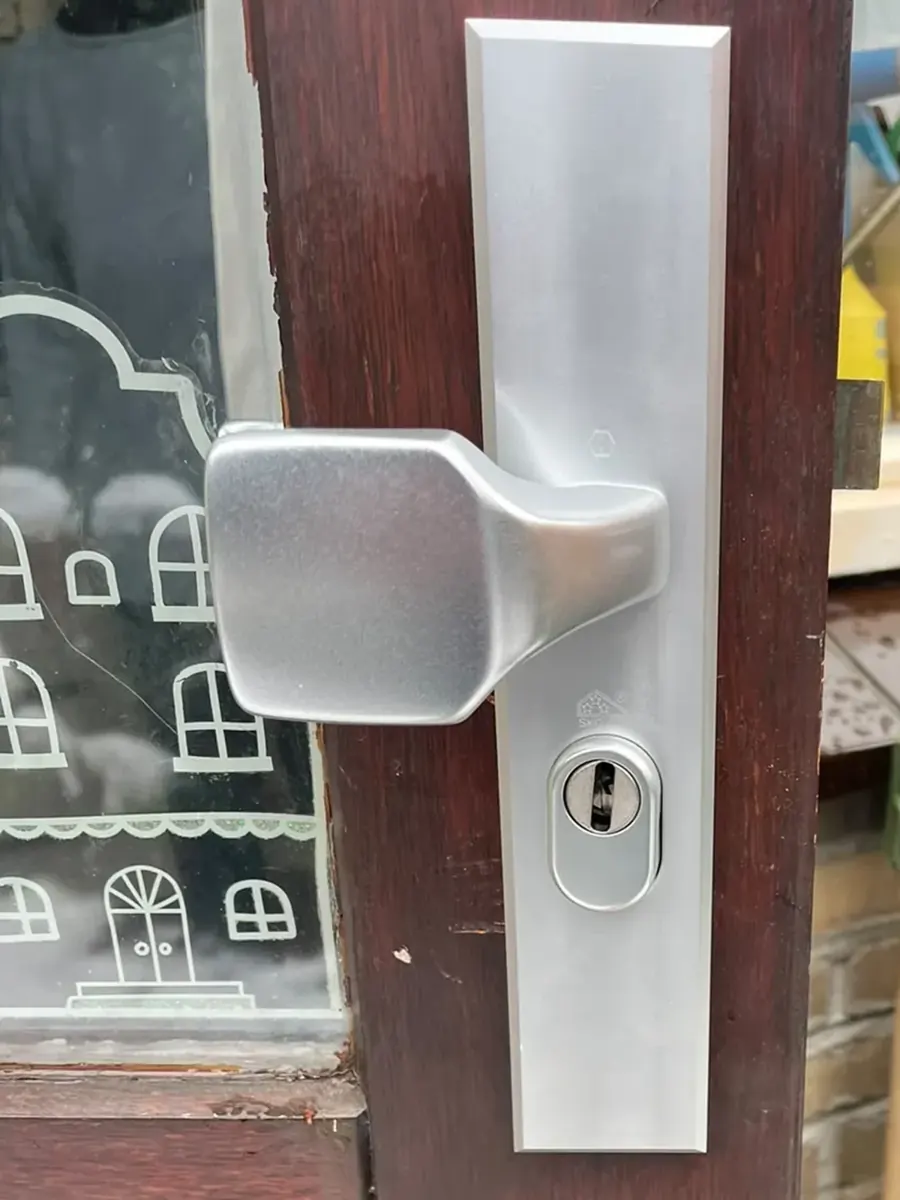 Aluminium veiligheidsbeslag met vaste knop en een kerntrekrozet om de cilinder, op een houten deur met glas