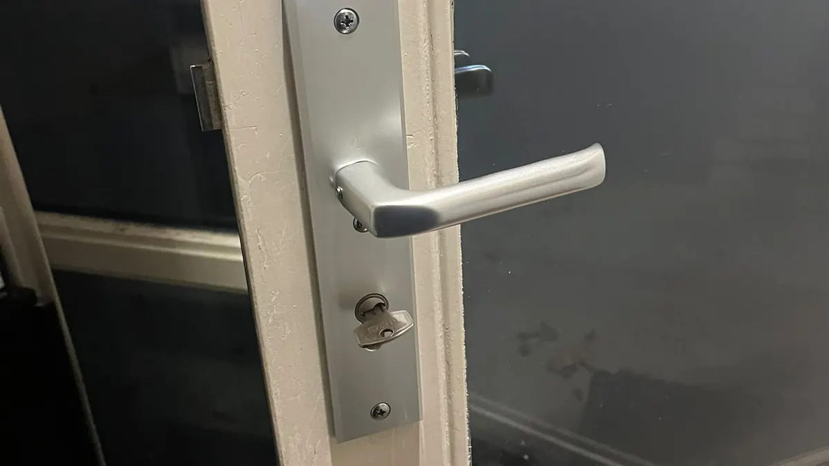 Aluminium langschild met deurkruk en sleutel in de cilinder op een deur met glas
